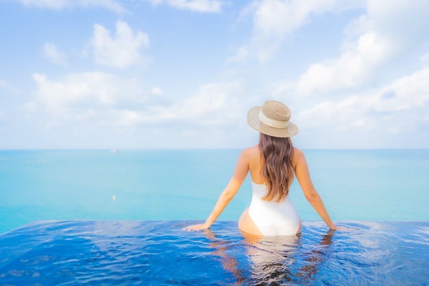 Portrait belle jeune femme asiatique se détendre sourire loisirs autour de la piscine extérieure avec mer océan en vacances de voyage
