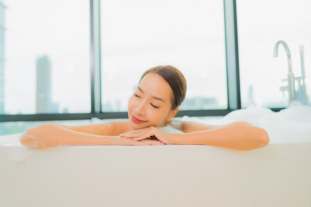 Portrait belle jeune femme asiatique se détendre sourire loisirs dans la baignoire à l'intérieur de la salle de bain