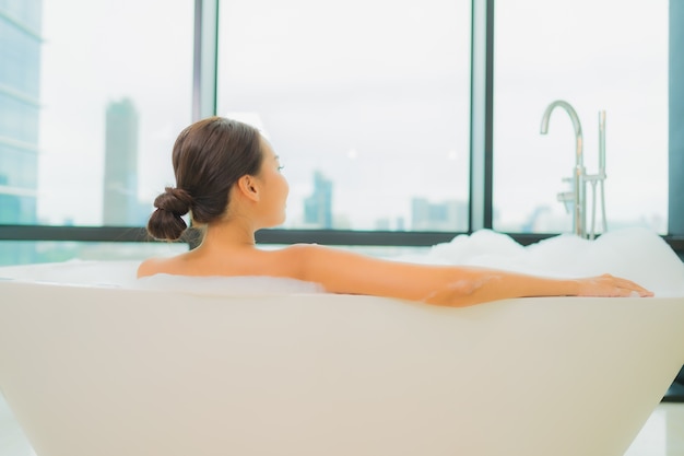 Portrait belle jeune femme asiatique se détendre sourire loisirs dans la baignoire à l'intérieur de la salle de bain