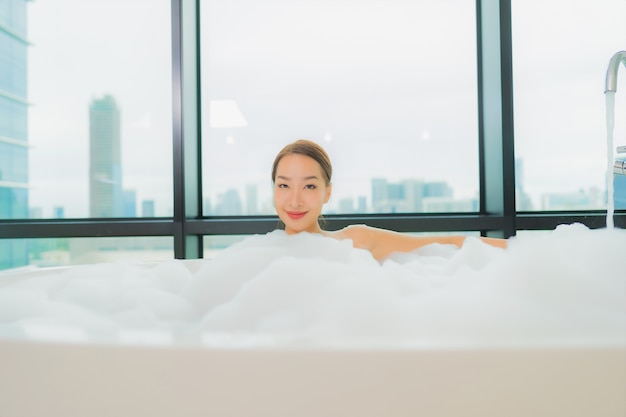 Portrait belle jeune femme asiatique se détendre sourire loisirs dans la baignoire à l'intérieur de la salle de bain