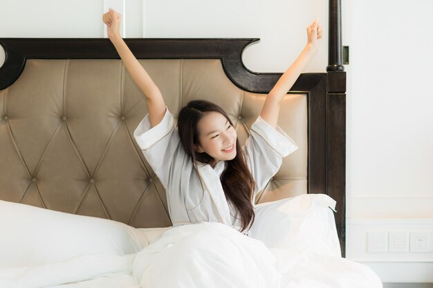 Portrait belle jeune femme asiatique se réveiller avec heureux et sourire sur le lit à l&#39;intérieur de la chambre