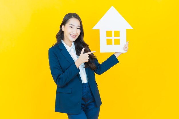 Portrait belle jeune femme asiatique avec signe de papier maison ou maison sur jaune