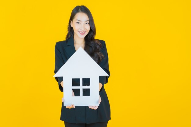 Portrait belle jeune femme asiatique avec signe de papier maison ou maison sur jaune