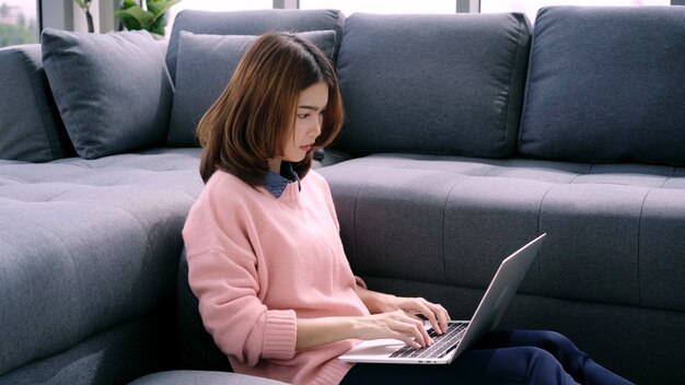 Portrait de la belle jeune femme asiatique souriante attrayante à l&#39;aide d&#39;un ordinateur ou un ordinateur portable en position couchée sur le canapé