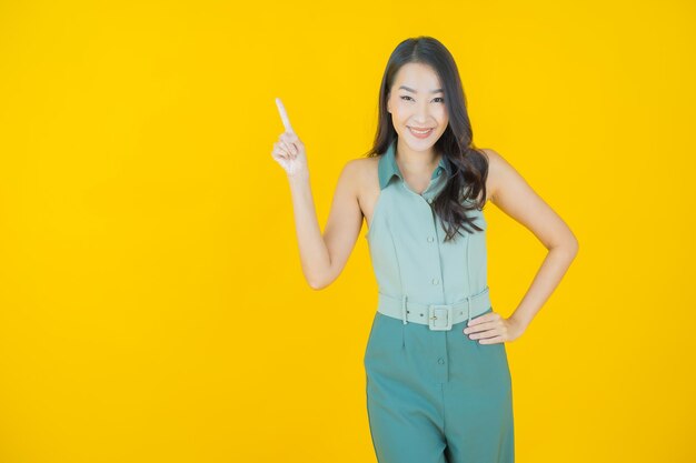 Portrait d'une belle jeune femme asiatique souriante faisant une action sur un mur jaune