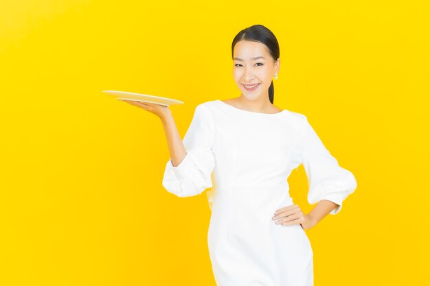 Portrait belle jeune femme asiatique sourire avec assiette vide sur jaune