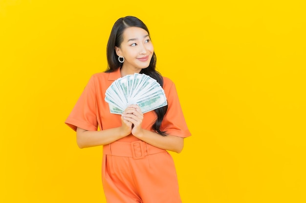 Portrait belle jeune femme asiatique sourire avec beaucoup d'argent et d'argent sur jaune