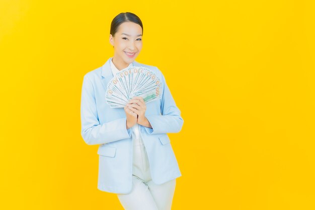 Portrait belle jeune femme asiatique sourire avec beaucoup d'argent et d'argent sur jaune