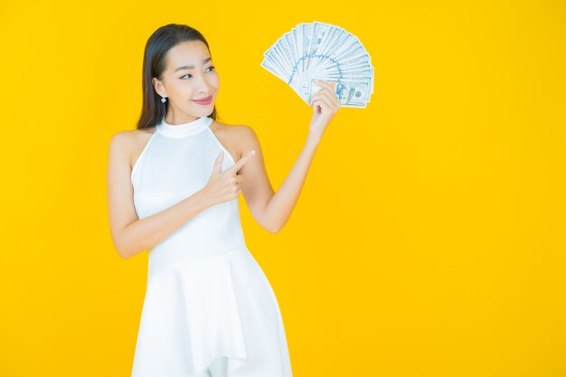 Portrait belle jeune femme asiatique sourire avec beaucoup d'argent et d'argent sur jaune