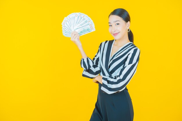 Portrait belle jeune femme asiatique sourire avec beaucoup d'argent et d'argent sur jaune