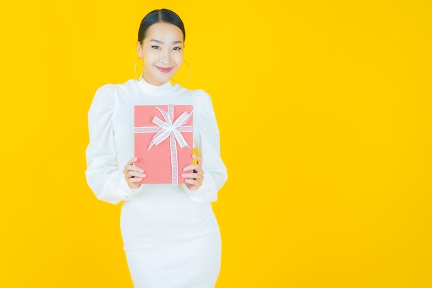 Portrait belle jeune femme asiatique sourire avec boîte-cadeau rouge sur jaune