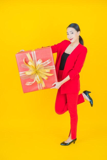 Portrait belle jeune femme asiatique sourire avec boîte-cadeau rouge sur jaune