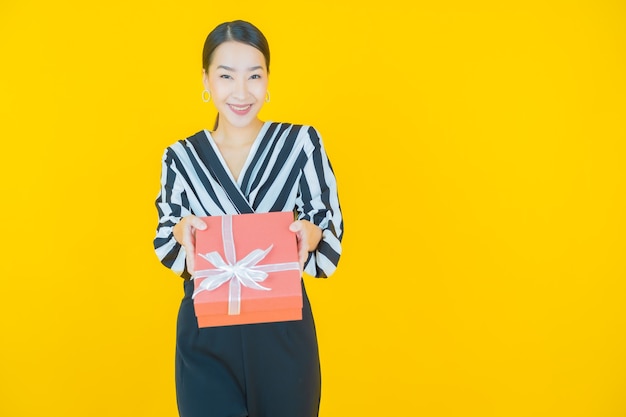 Portrait belle jeune femme asiatique sourire avec boîte-cadeau rouge sur jaune