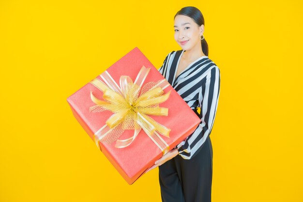 Portrait belle jeune femme asiatique sourire avec boîte-cadeau rouge sur jaune