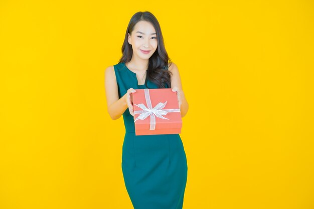 Portrait belle jeune femme asiatique sourire avec boîte-cadeau rouge sur jaune