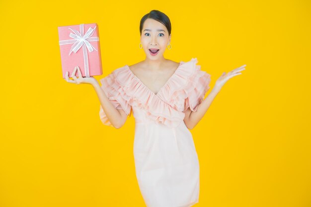 Portrait belle jeune femme asiatique sourire avec boîte-cadeau rouge sur jaune