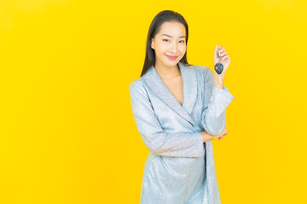 Portrait belle jeune femme asiatique sourire avec clé de voiture sur mur jaune