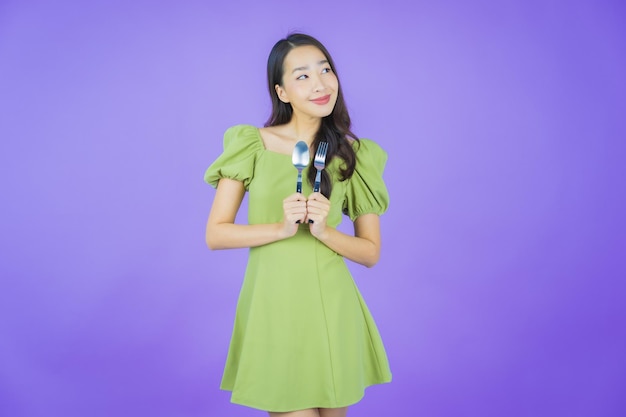 Portrait belle jeune femme asiatique sourire avec cuillère et fourchette sur fond de couleur