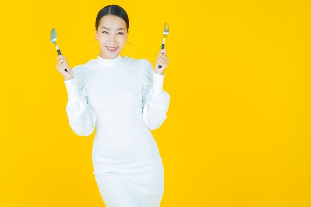 Portrait belle jeune femme asiatique sourire avec cuillère et fourchette sur jaune