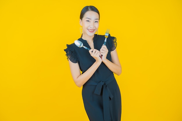 Portrait belle jeune femme asiatique sourire avec cuillère et fourchette sur jaune