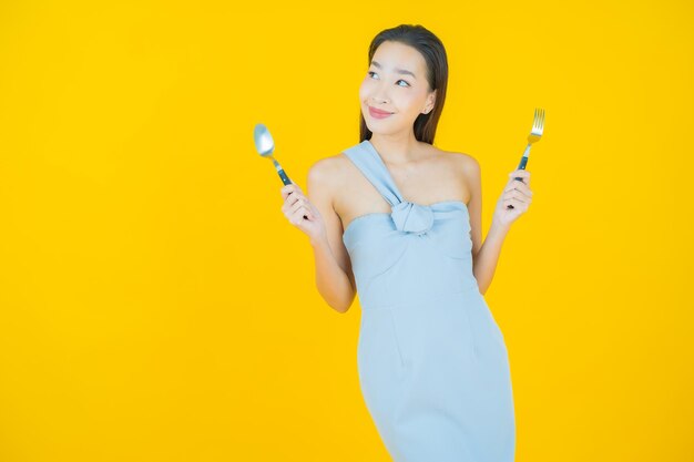 Portrait belle jeune femme asiatique sourire avec cuillère et fourchette sur jaune