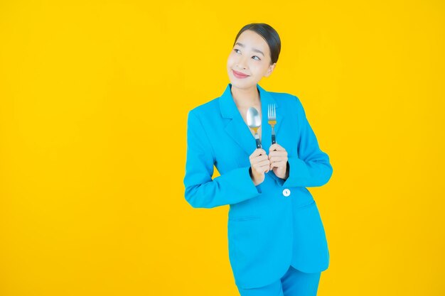 Portrait belle jeune femme asiatique sourire avec cuillère et fourchette sur jaune