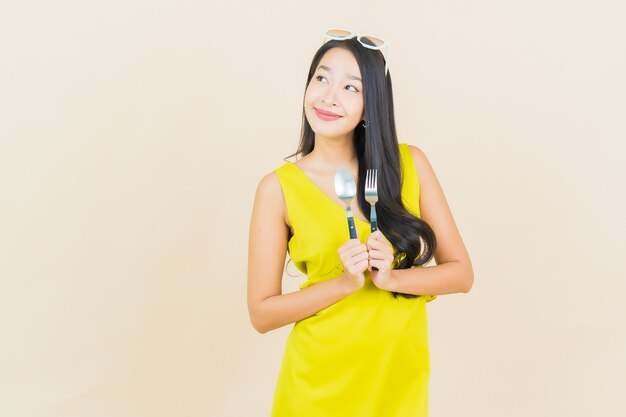 Portrait belle jeune femme asiatique sourire avec cuillère et fourchette sur le mur de couleur