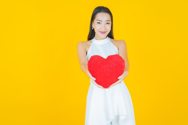 Portrait belle jeune femme asiatique sourire avec forme d'oreiller coeur sur jaune