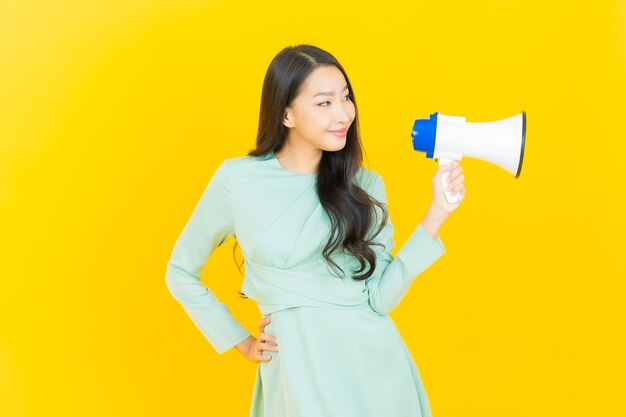 Portrait belle jeune femme asiatique sourire avec mégaphone sur jaune