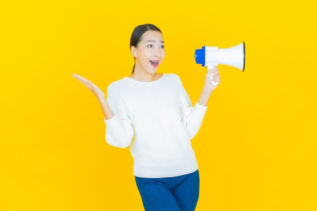 Portrait belle jeune femme asiatique sourire avec mégaphone sur jaune