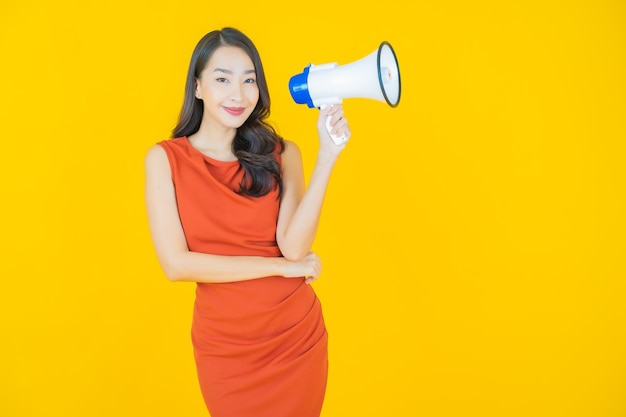 Portrait belle jeune femme asiatique sourire avec mégaphone sur jaune