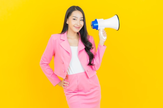 Portrait belle jeune femme asiatique sourire avec mégaphone sur mur de couleur jaune