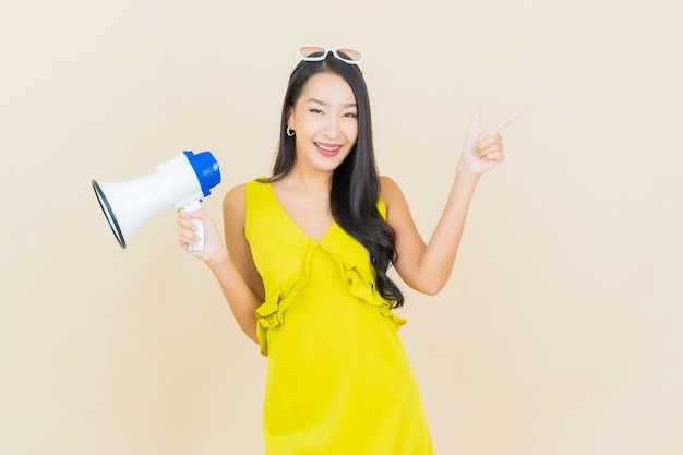 Portrait belle jeune femme asiatique sourire avec mégaphone sur le mur de couleur