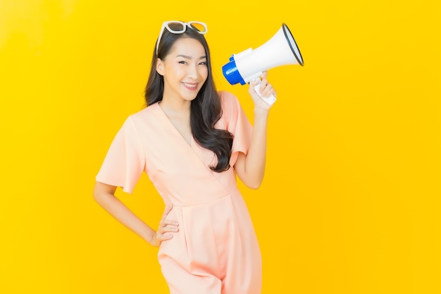 Portrait belle jeune femme asiatique sourire avec mégaphone sur mur de couleur