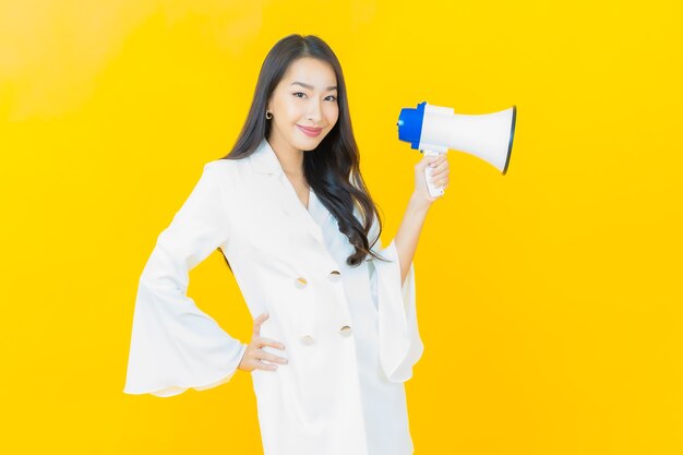 Portrait de la belle jeune femme asiatique sourire avec mégaphone sur mur jaune