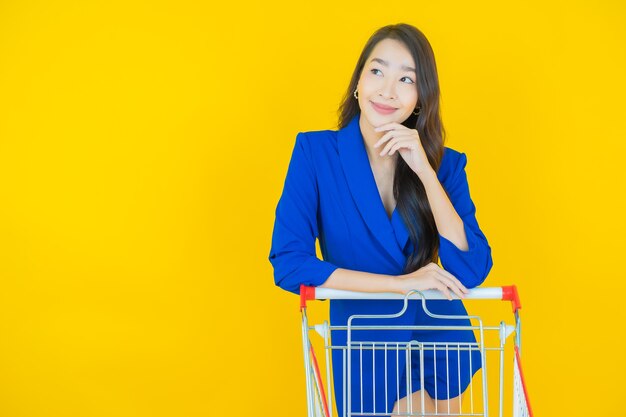 Portrait belle jeune femme asiatique sourire avec panier d'épicerie du supermarché sur jaune