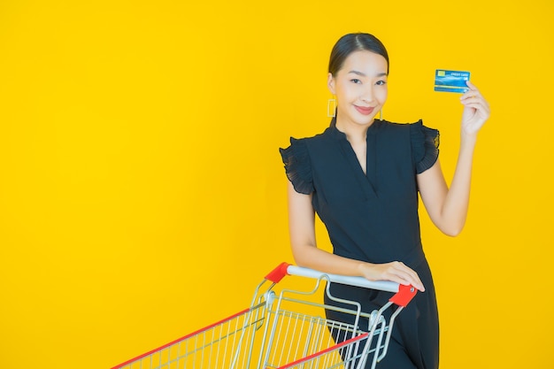 Portrait belle jeune femme asiatique sourire avec panier d'épicerie du supermarché sur jaune