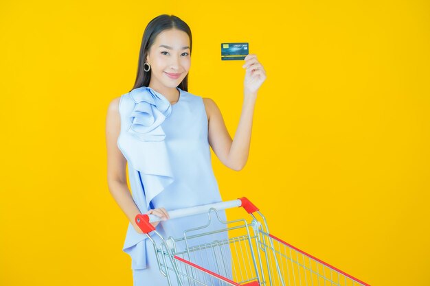 Portrait belle jeune femme asiatique sourire avec panier d'épicerie du supermarché sur jaune