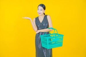 Photo gratuite portrait belle jeune femme asiatique sourire avec panier d'épicerie du supermarché sur jaune