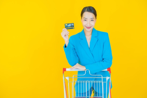 Portrait belle jeune femme asiatique sourire avec panier d'épicerie du supermarché sur jaune