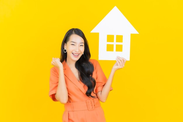Portrait belle jeune femme asiatique sourire avec panneau de papier à la maison sur jaune
