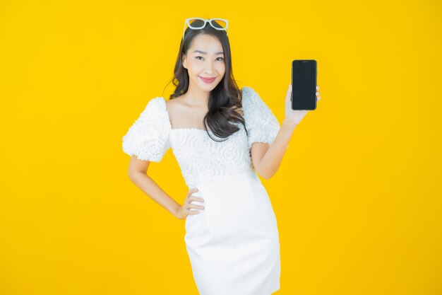 Portrait belle jeune femme asiatique sourire avec téléphone mobile intelligent sur jaune