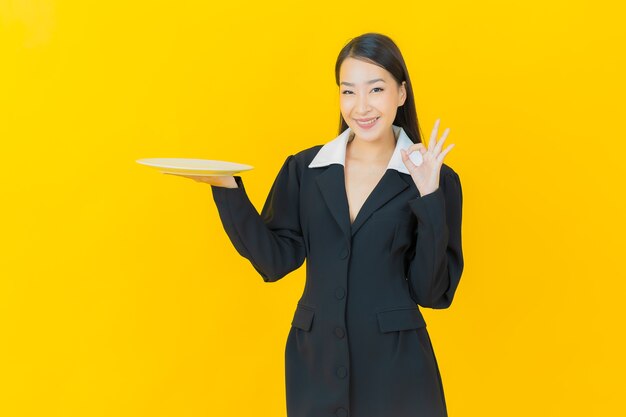 Portrait belle jeune femme asiatique sourit avec une assiette vide sur un mur de couleur