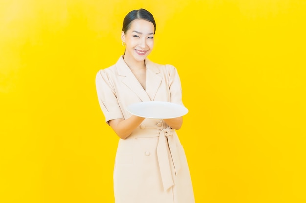 Portrait belle jeune femme asiatique sourit avec une assiette vide sur un mur de couleur