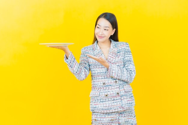 Portrait belle jeune femme asiatique sourit avec une assiette vide sur un mur de couleur