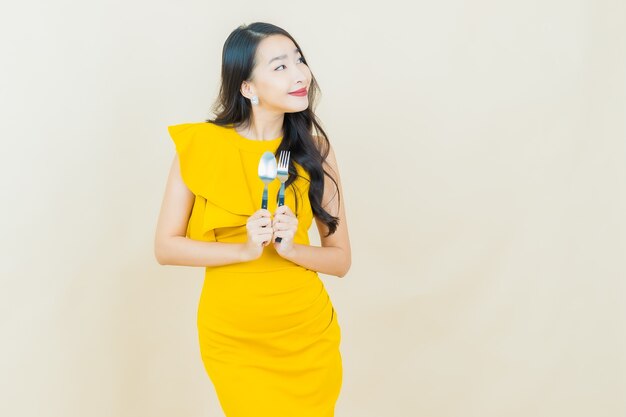 Portrait belle jeune femme asiatique sourit avec cuillère et fourchette sur mur beige
