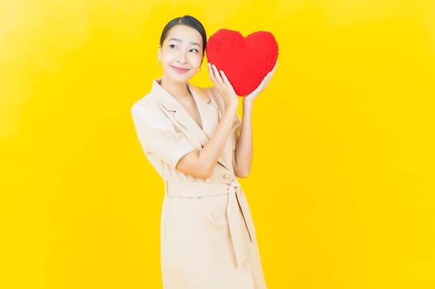 Portrait belle jeune femme asiatique sourit avec forme d'oreiller coeur sur mur de couleur