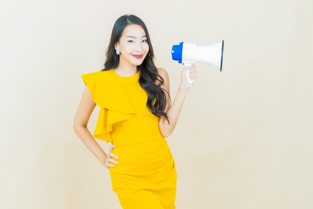 Portrait belle jeune femme asiatique sourit avec mégaphone sur mur beige