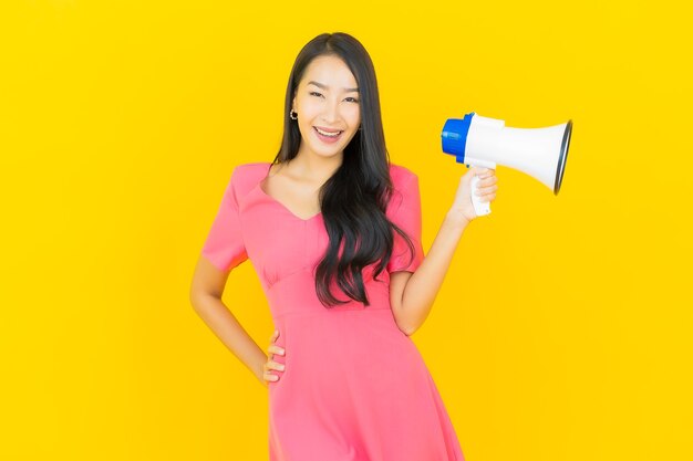 Portrait belle jeune femme asiatique sourit avec mégaphone sur mur jaune