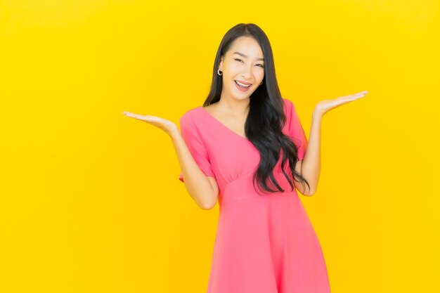 Portrait de la belle jeune femme asiatique sourit en robe rose sur mur jaune